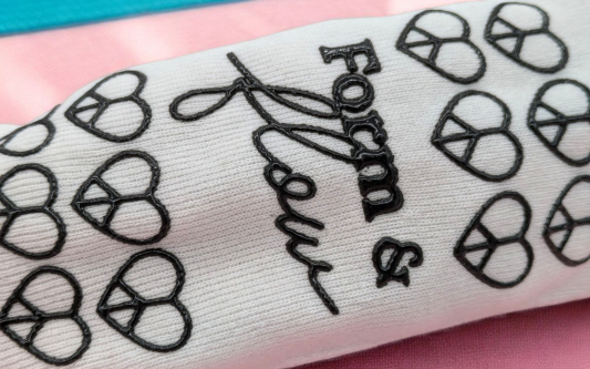 A white pilates sock with a black patterned grip on the sole. The pattern is hearts with the words