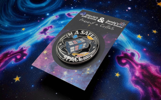 circular pin badge with a TARDIS in the middle made up of the trans pride flag colours. Around the TARDIS reads the words