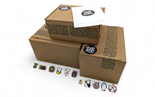 A pile of Made by Cooper branded boxes and envelopes surrounded by pin badges to show people how and why packaging for pin badges is essential.